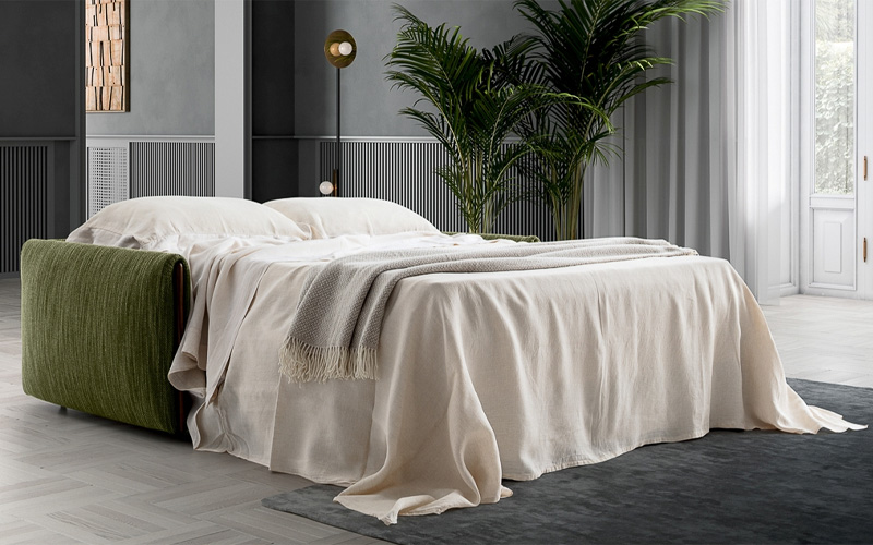 A modern sofa bed dressed in neutral linens with green upholstery in a contemporary gray and white room.