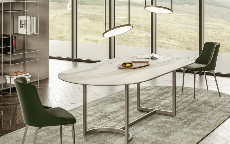 Minimalist interior with oval marble table, green chairs, pendant lights, and scenic window view.