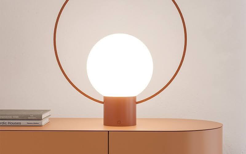 A minimalist circular globe lamp with a thin metal frame on an orange contemporary sideboard.