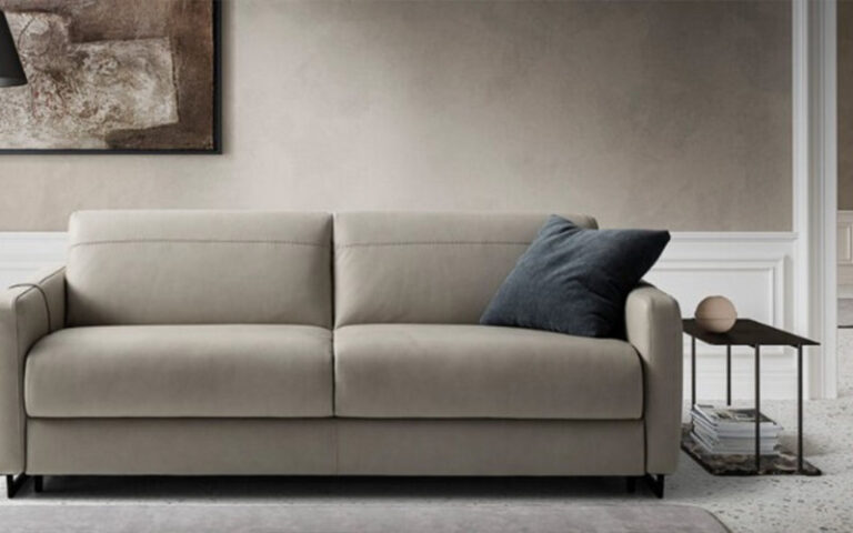 A modern, cream-colored leather sofa bed in a minimalist living room