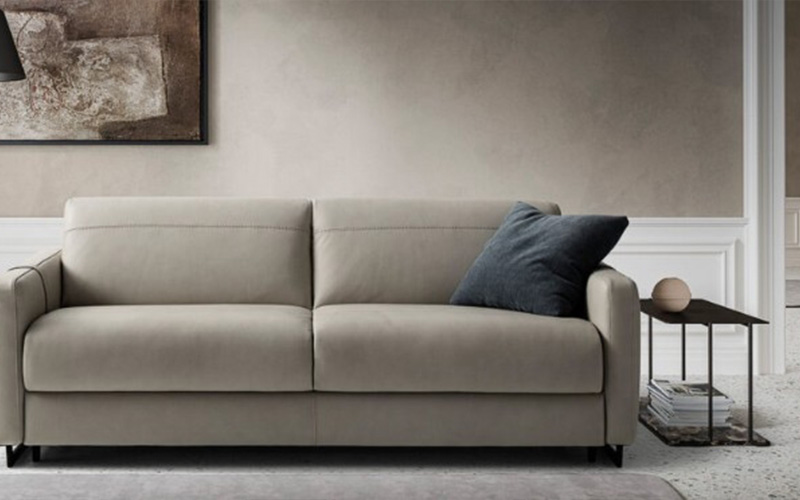 A modern, cream-colored leather sofa bed in a minimalist living room